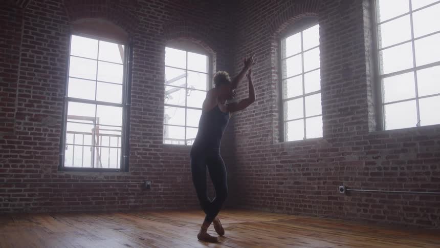 A ballet dancer gracefully performs a routine in a rustic brick loft with large bright windows