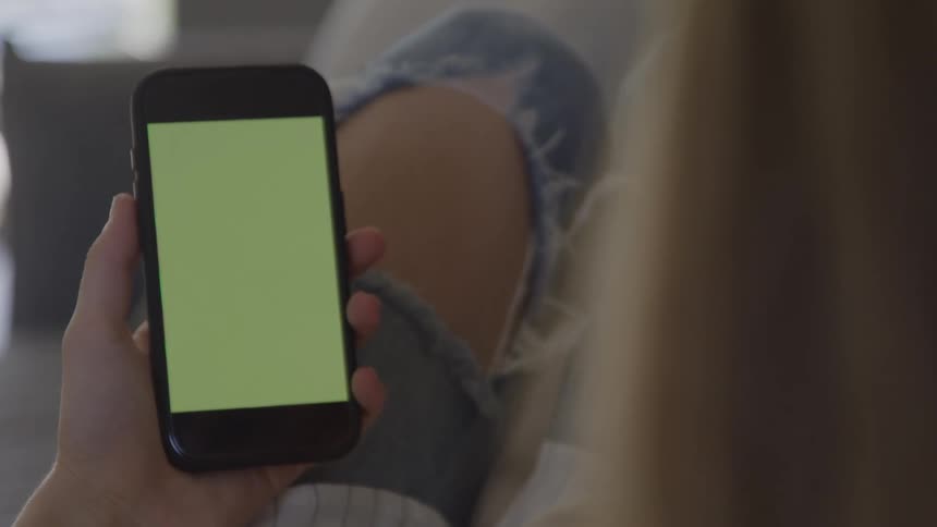 A person holds up a smartphone with a green screen while relaxing on a couch