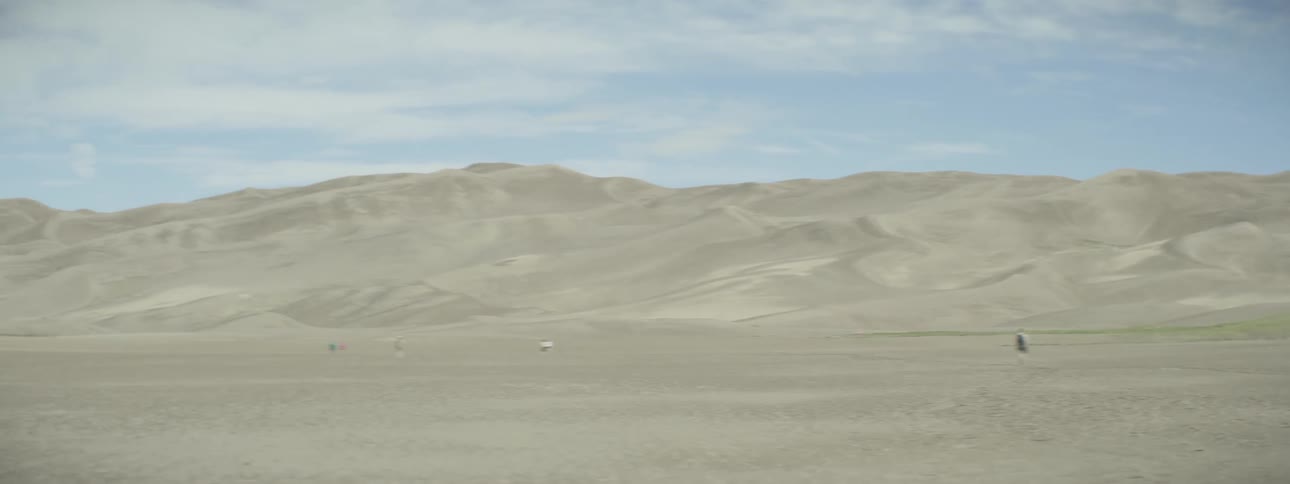 People walking in a sandy field near hills