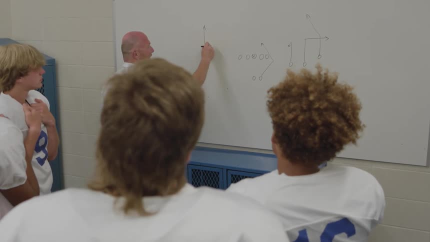 Coach explains a play on a whiteboard to football players