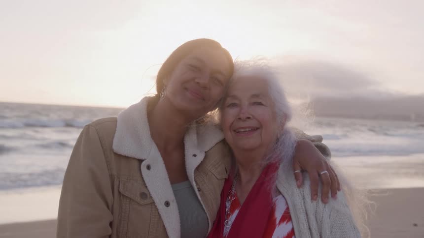A young woman and the elderly woman hugging each other on the beach sand