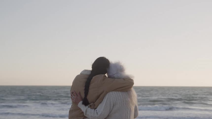 Grandmother and granddaughter are hugging as they watch the ocean