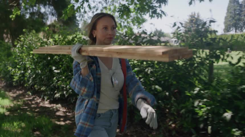 The woman is carrying plywood in her yard
