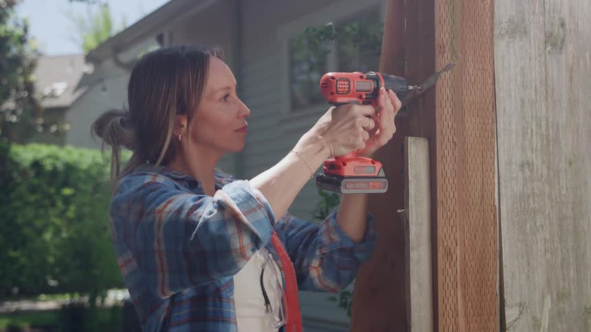 An interior designer drills into a wooden beam outside a house