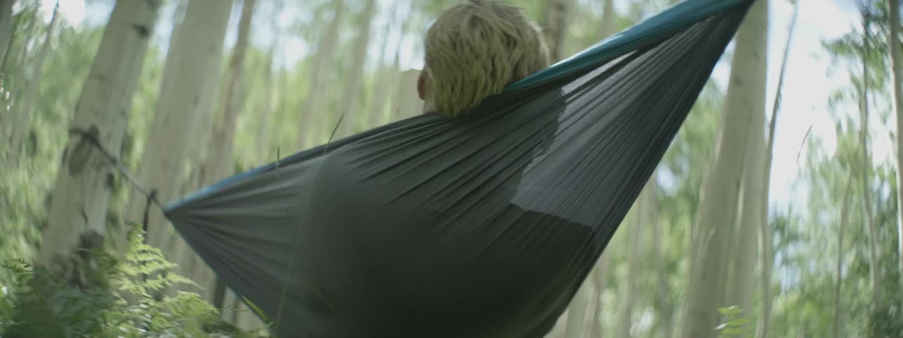 A man is lying in a hammock reading