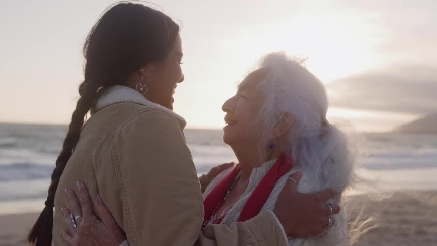 The women smile at each other and hug on the beach