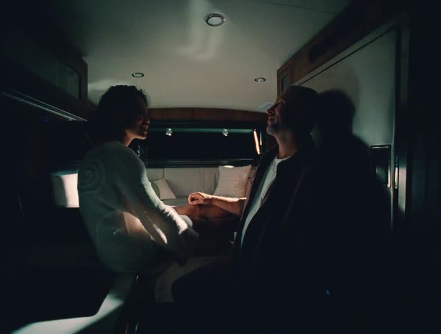 A couple sits and talks inside a dimly lit vehicle