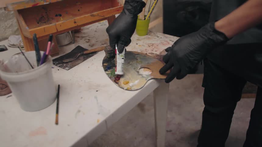 A person is squeezing paint onto a palette in an art studio