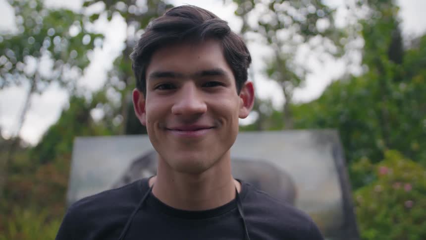 The man smiles in front of his painting outside