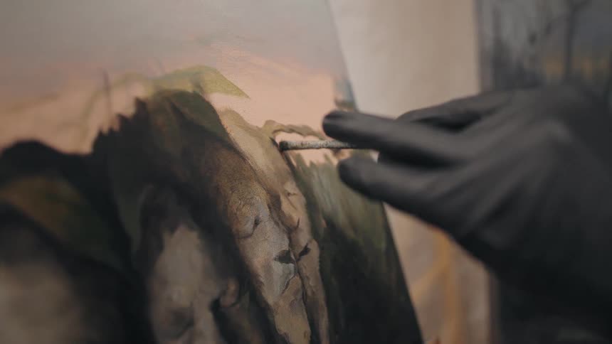 A painter in a black glove carefully adding details to a canvas with a fine brush