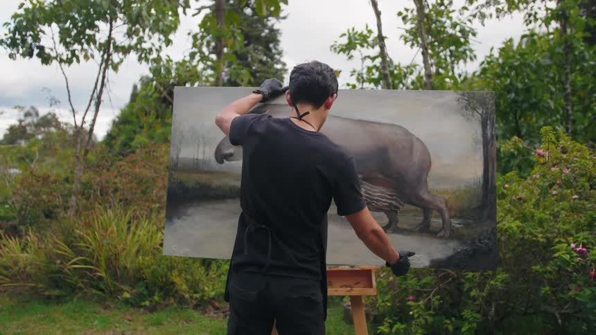 An artist places a large finished painting of a tapir and its calf on an easel in a garden