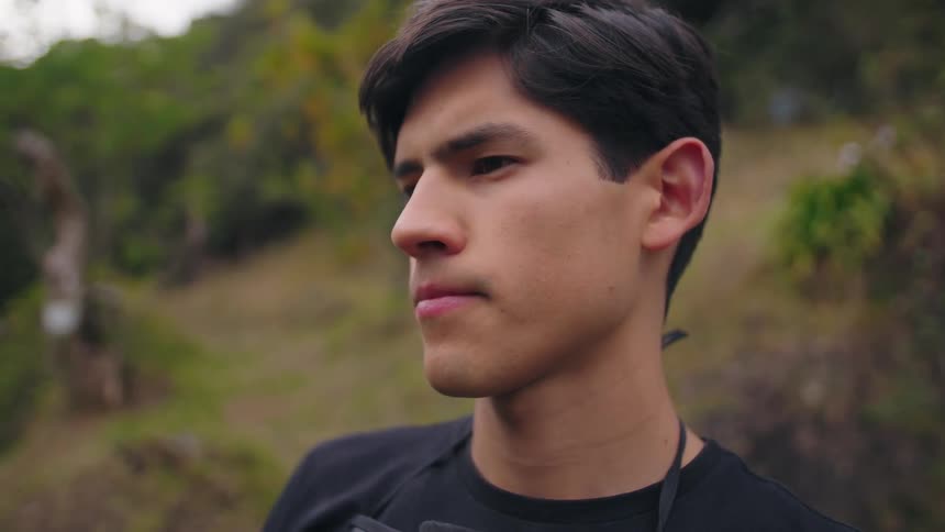 Man with short hair wears black shirt while looking sideways in a setting with greenery