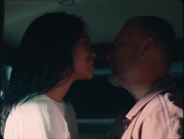In a dimly lit intimate close up a man and woman face each other their features highlighted by dramatic flickering light