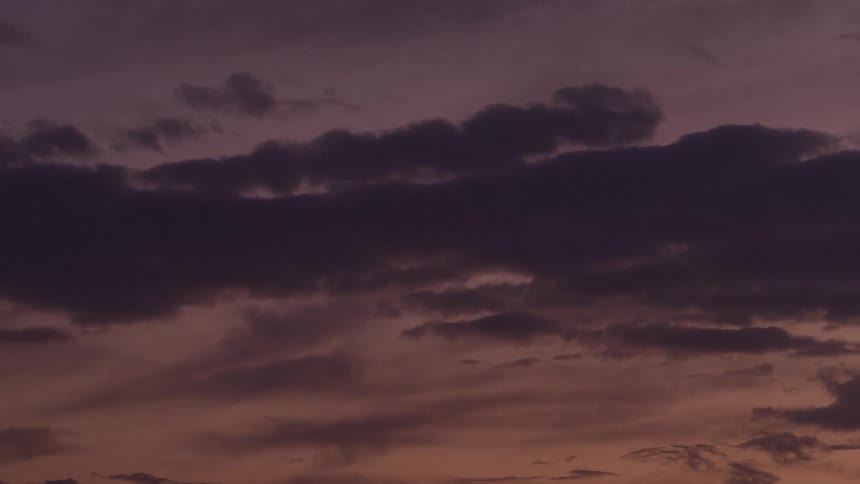 Clouds drift and darken across the screen as the sky transitions quickly from pink and purple hues to a deep black night sky