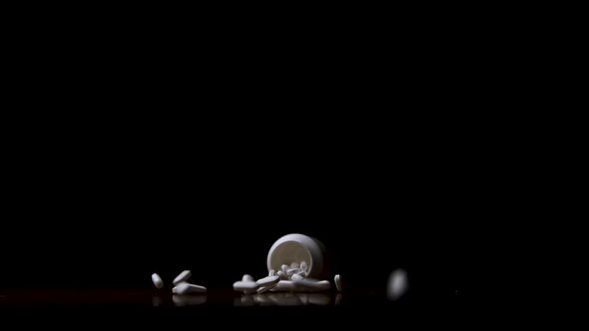 White bottle tipped over with white capsules scattered across dark surface
