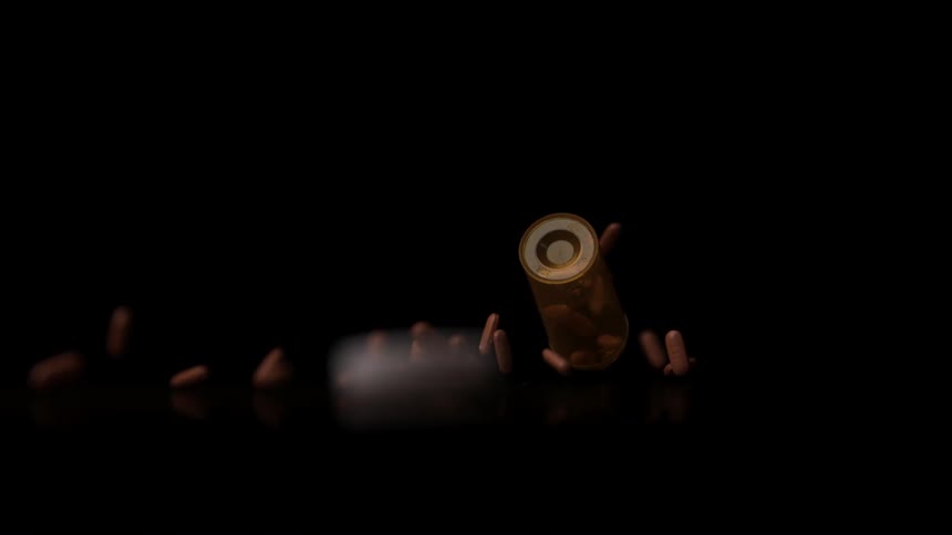 Amber bottle tipped over with brown capsules scattered against black background
