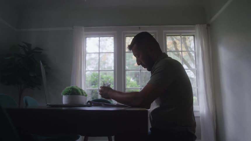 Man reviews document while using laptop in a naturally lit room