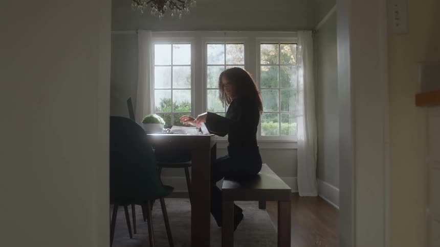 Woman sitting at a table writing near a bright window