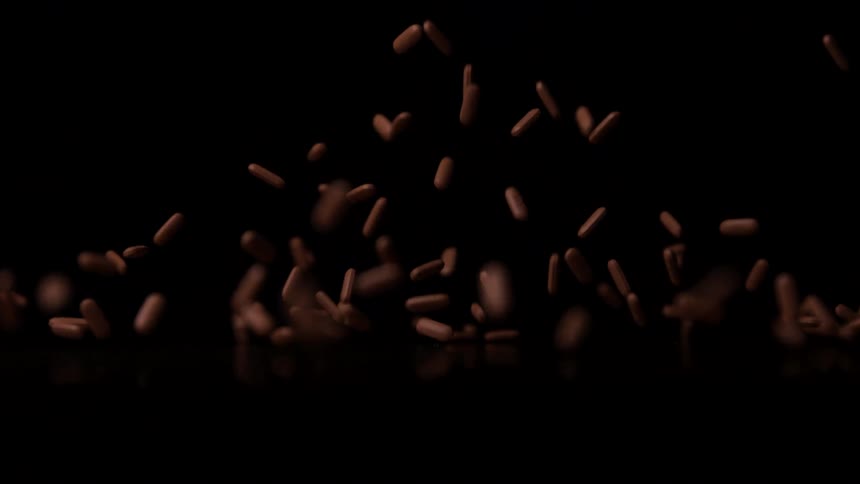 Brown capsules falling in midair against black background