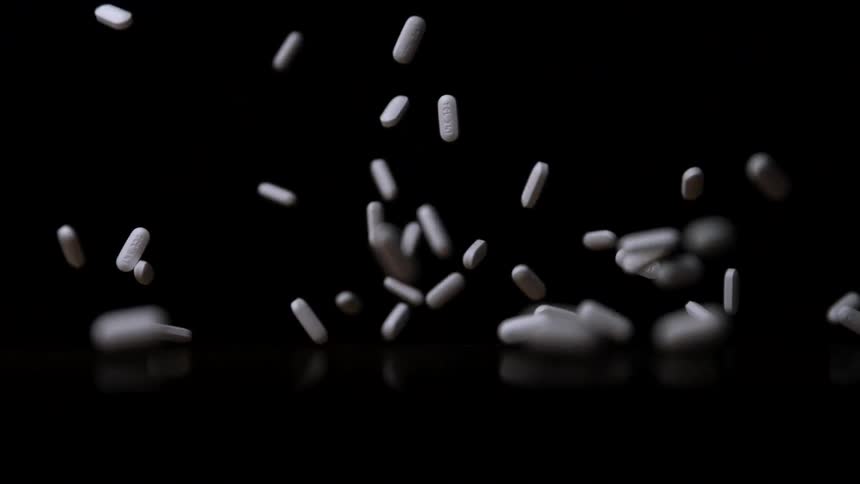 White capsules falling freely against black background