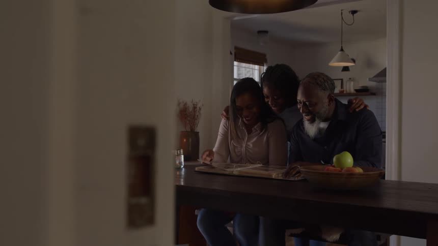 Family gathered at the table browses photo album in home setting with warm lighting