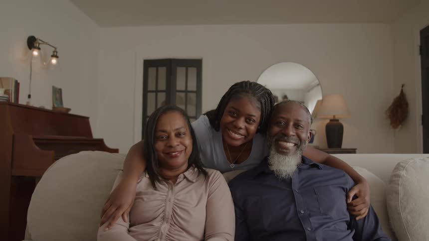 A happy family sits close together on a couch in a cozy living room
