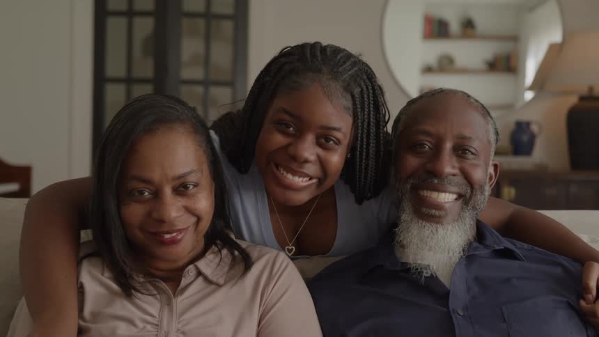 A smiling family sits together on a couch in a bright living room