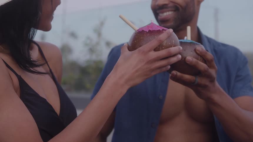 Couple toasts with drinks served in decorated coconuts outdoors