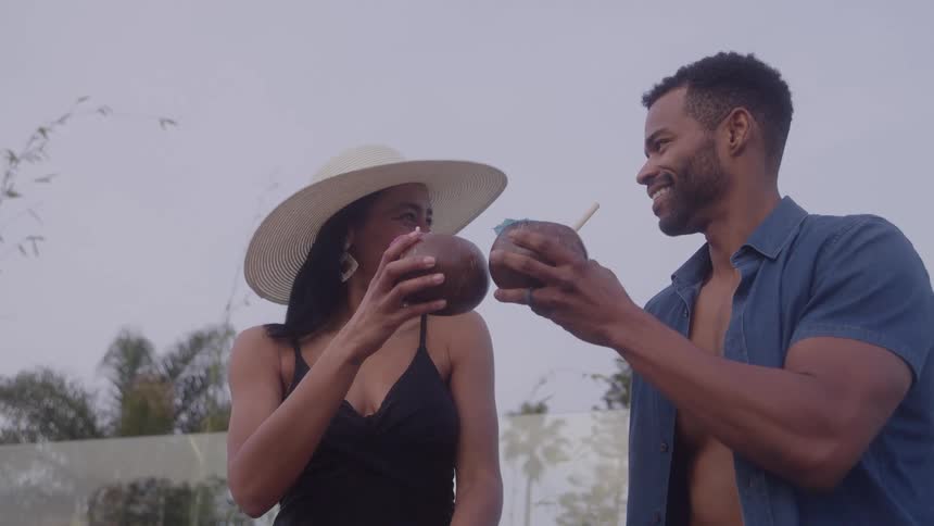 A smiling couple clinks coconut drinks together while relaxing outdoors