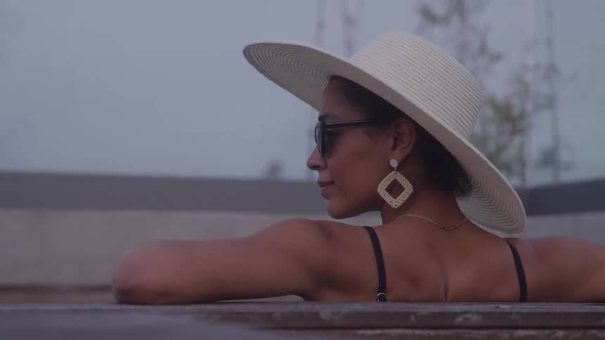Person relaxes in outdoor pool or hot tub wearing white hat and dark sunglasses