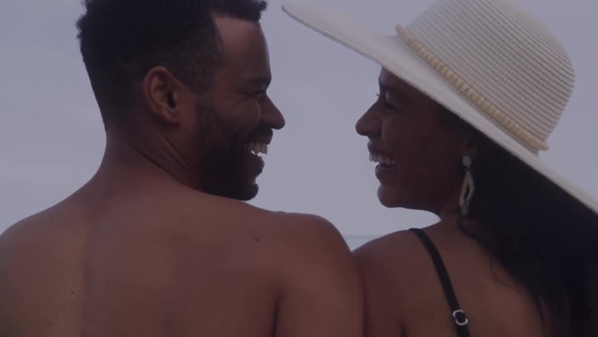 A couple enjoys a fun time together on the beach the man shirtless and the woman wearing a hat standing side by side under the sun