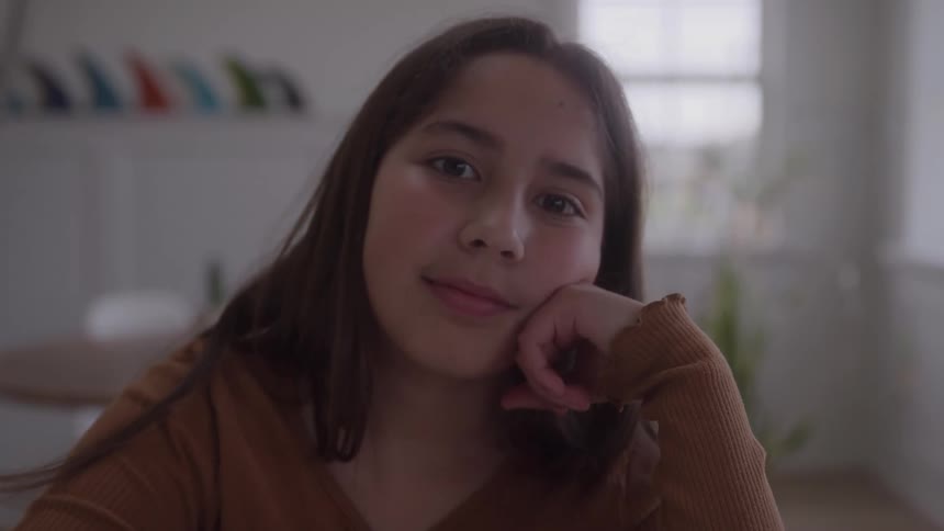 A teenage girl is sitting and thinking with her head resting on her hand