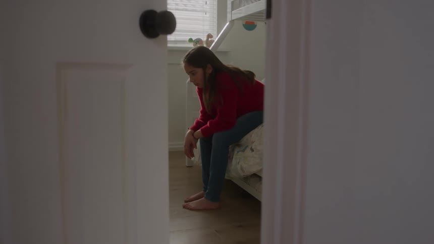 Girl sitting on the edge of the bed with a thoughtful expression