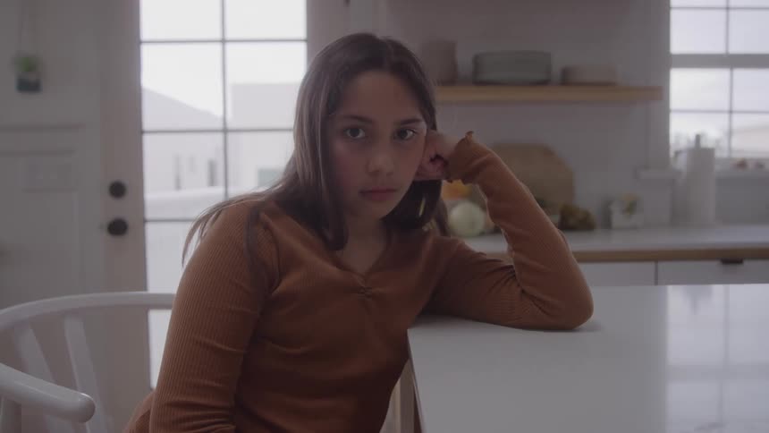 Person in brown top rests head on hand while staring directly in welllit home setting
