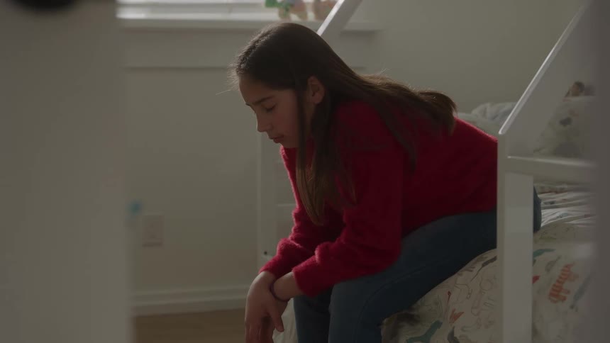 Girl sitting on the edge of the bed in a sunlit room appearing thoughtful