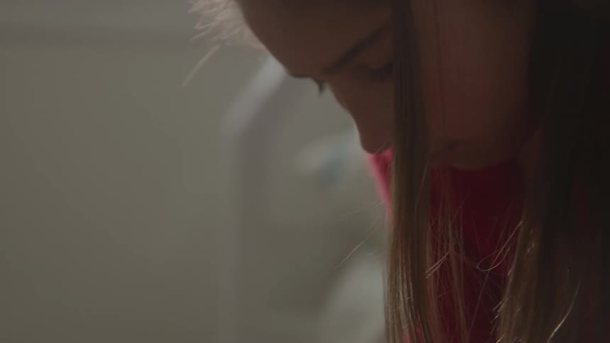 A closeup side profile shot of a young person in a red sweater with long brown hair covering their face looking down or away with a thoughtful expression the lighting is soft and diffused highlighting the silhouette of their profile