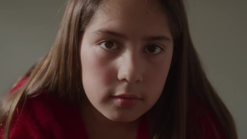 Girl with long brown hair stares with a neutral expression