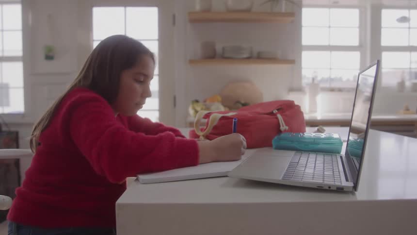 A girl writes near a laptop