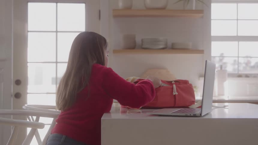 Young person studies with notebook and laptop on counter in naturally lit home setting