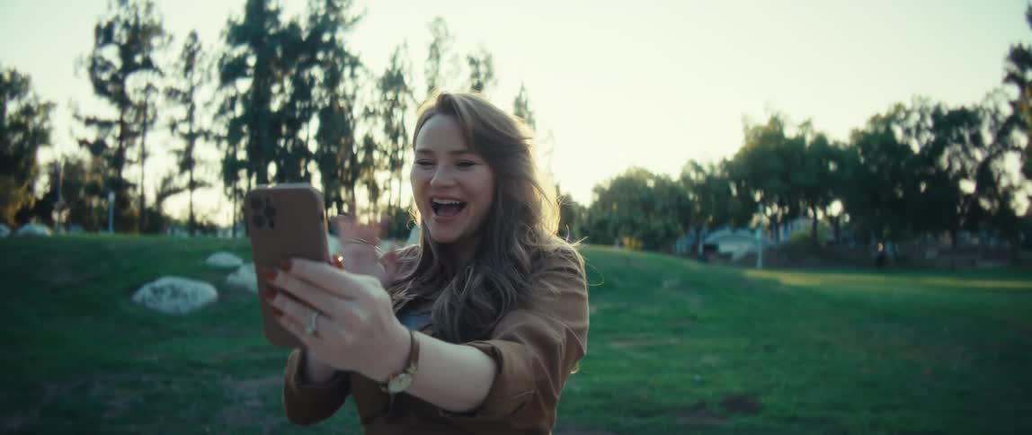The woman is smiling and waving at her cell phone