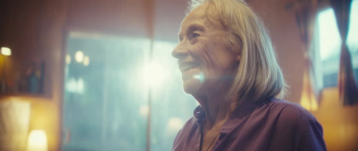 A closeup sideprofile shot shows an elderly man smiling broadly as he turns his head toward an offcamera person the soft warm interior lighting highlights his white hair and wrinkled face