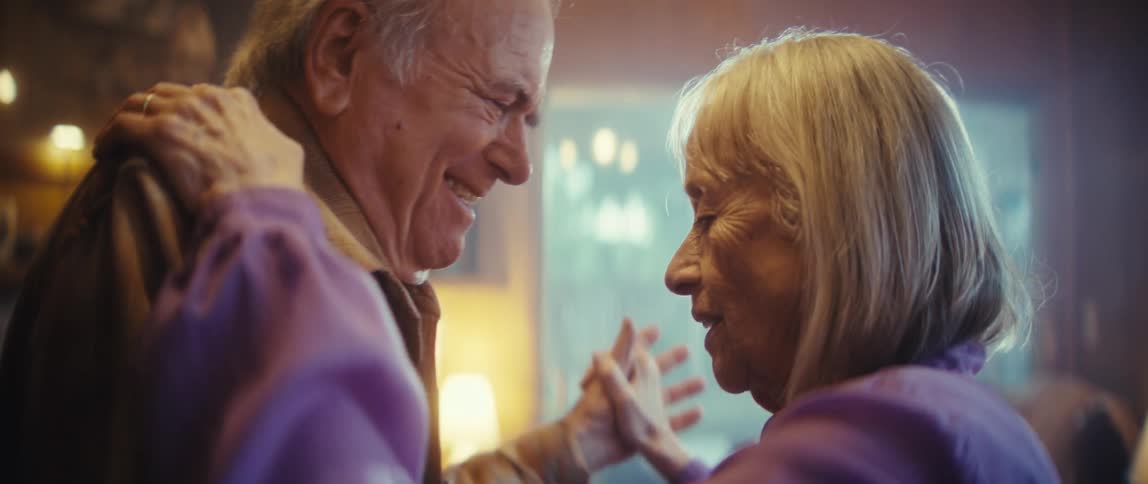 A closeup shot focuses on an elderly couple slowdancing in a cozy softly lit room the mans hands are gently placed on the womans shoulder indicating a loving embrace