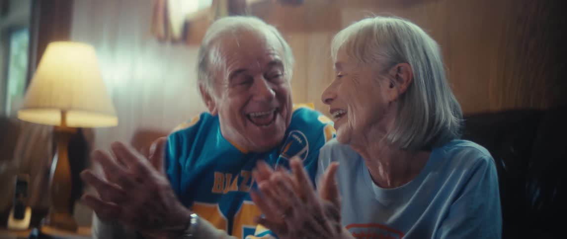 A man and woman are clapping and smiling as they sit on a couch