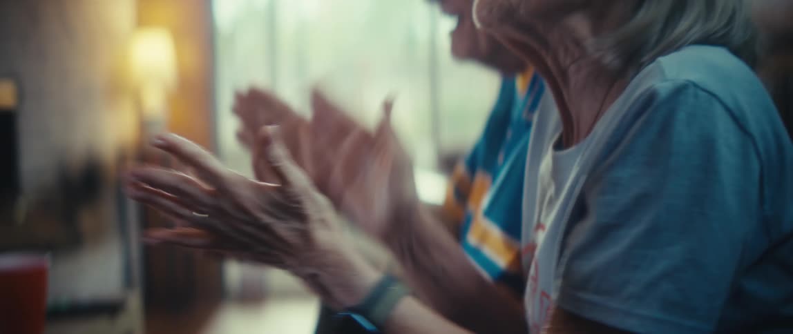 An elderly couple is clapping and singing as they sit on their couch