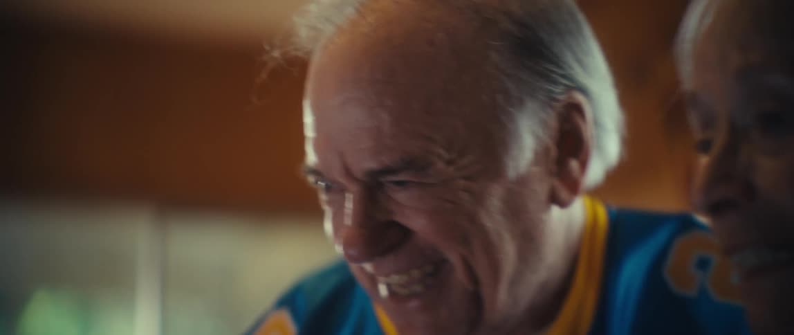 N elderly man smiles with a wide mouth while touching an elderly womans hand and then the elderly woman opens her mouth and yells loudly showing an intense emotional reaction