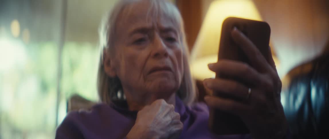 An elderly woman looks upset as she looks away frm her phone