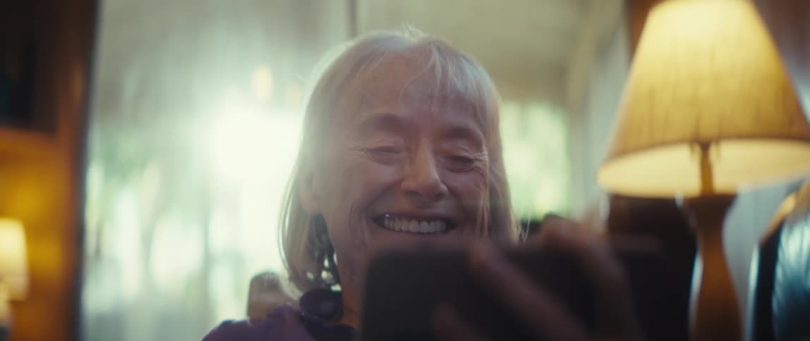 A woman is smiling as she looks at her cellphone