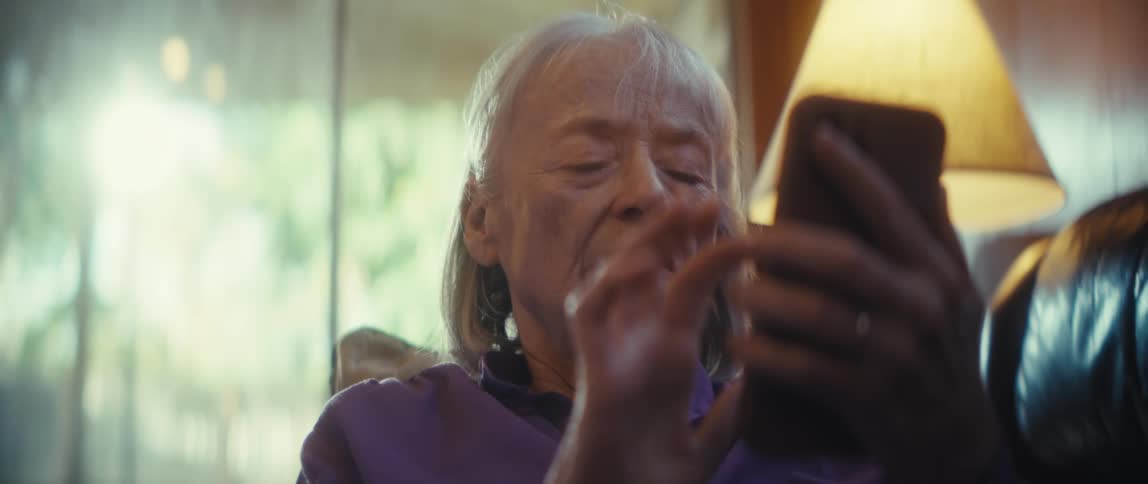 An elderly woman is using her finger to scroll on her cellphone