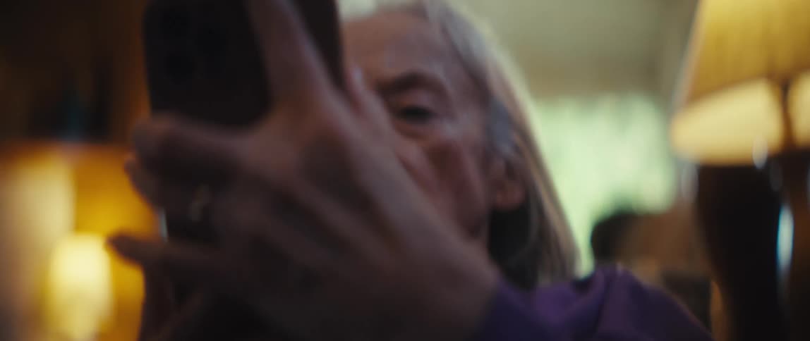 An elderly woman sitting and holding a cellphone looking at it