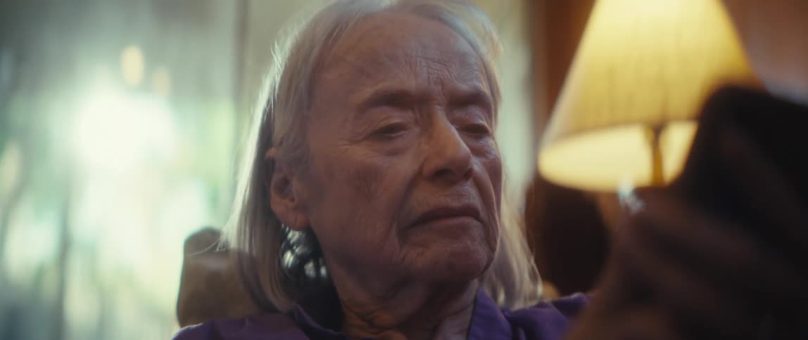 An elderly woman is sitting in a room looking at a cellphone